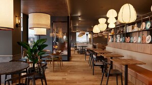 L’intérieur d’un restaurant moderne est agrémenté de tables et de chaises en bois, d’un éclairage suspendu et d’un mur où sont exposées des assiettes en céramique.