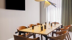Una sala de conferencias con una mesa larga, sillas, un televisor de pantalla plana y una lámpara colgante moderna.