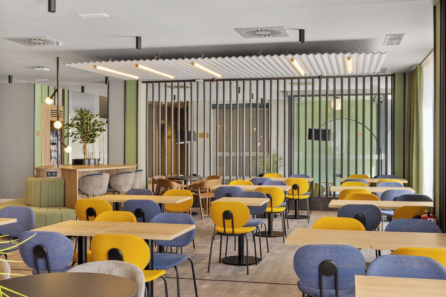 Un comedor moderno con varias mesas y sillas, una planta y vistas a través de un panel de vidrio.