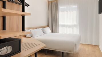 Una habitación de hotel con cama, escritorio con computadora, televisor y ventana con cortinas.