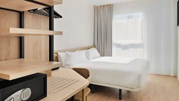Habitación de hotel con cama, escritorio, computadora, silla y ventana con cortinas.