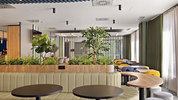 Un interior moderno con sofá, mesas redondas y sillas, destacando una pared de madera y plantas en macetas.