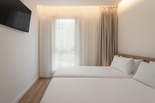 A hotel room with a bed, a TV mounted on the wall, and a window with curtains.