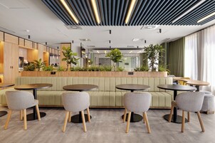 Ein modernes Café mit runden Tischen und gepolsterten Sitzgelegenheiten, mit einer Holztresen und Topfpflanzen.