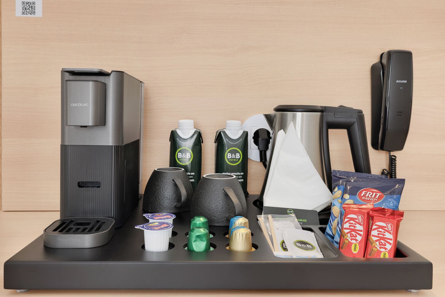 A hotel room's minibar setup with a coffee machine, two beverage dispensers, a phone, a tissue box, and snacks.