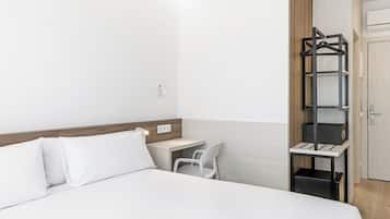 Una habitación de hotel con cama, escritorio, silla, armario y estante.