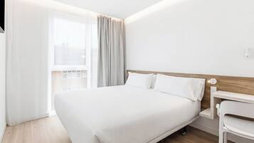 A modern hotel room with a large bed, a desk, and a window with curtains.