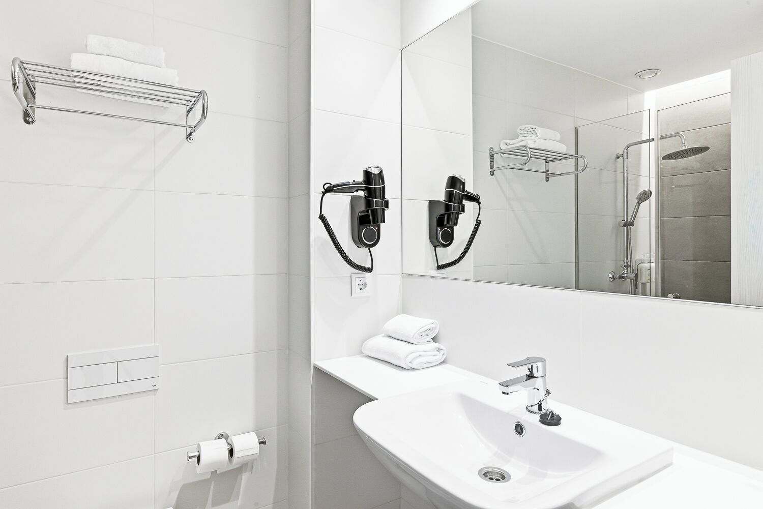 A modern bathroom with a white sink, a mirror, a towel rack, and a shower area.