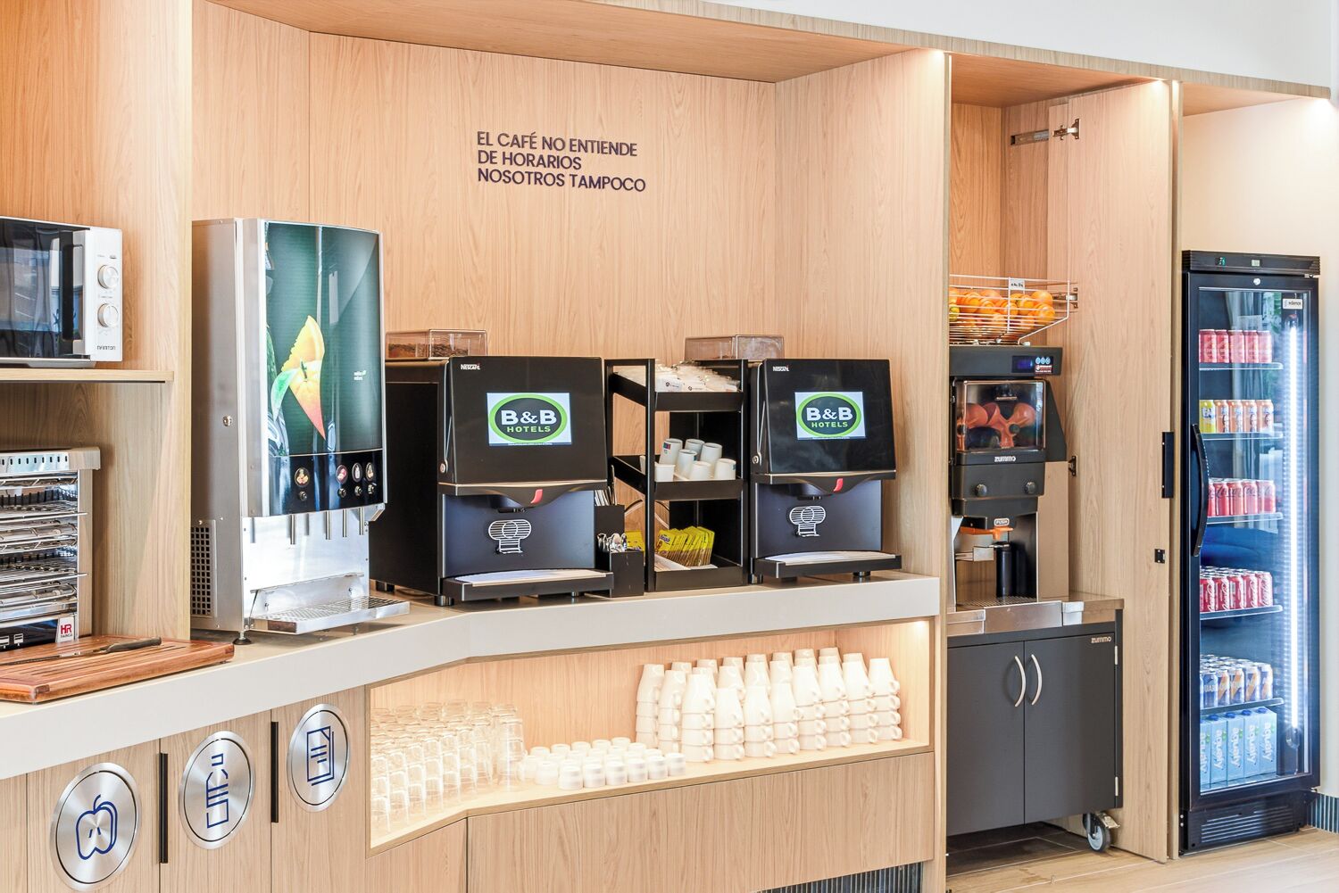 Una estación de café con varias máquinas de espresso, un refrigerador lleno de bebidas y una barra con vasos desechables.