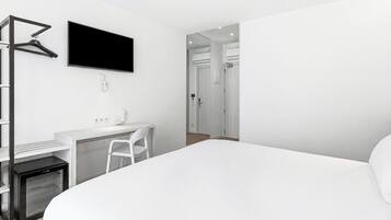 A modern hotel room with a bed, a desk with a chair, a TV mounted on the wall, and a wardrobe.