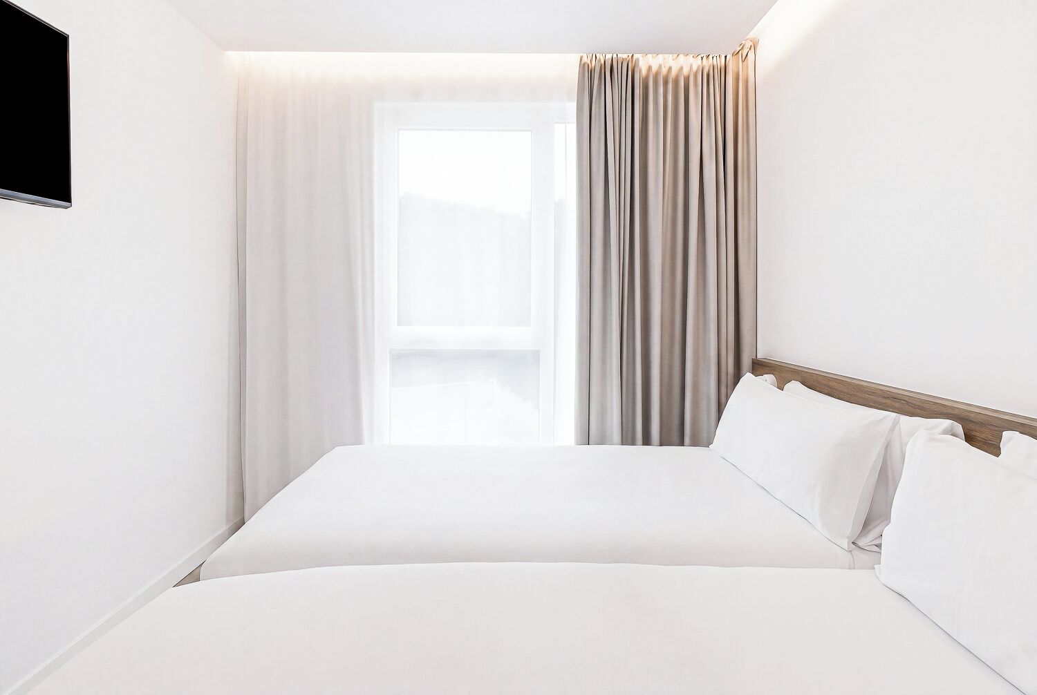 A hotel room with a bed, curtains, a TV, and a window.
