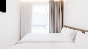 A hotel room with a bed, curtains, a TV, and a window.