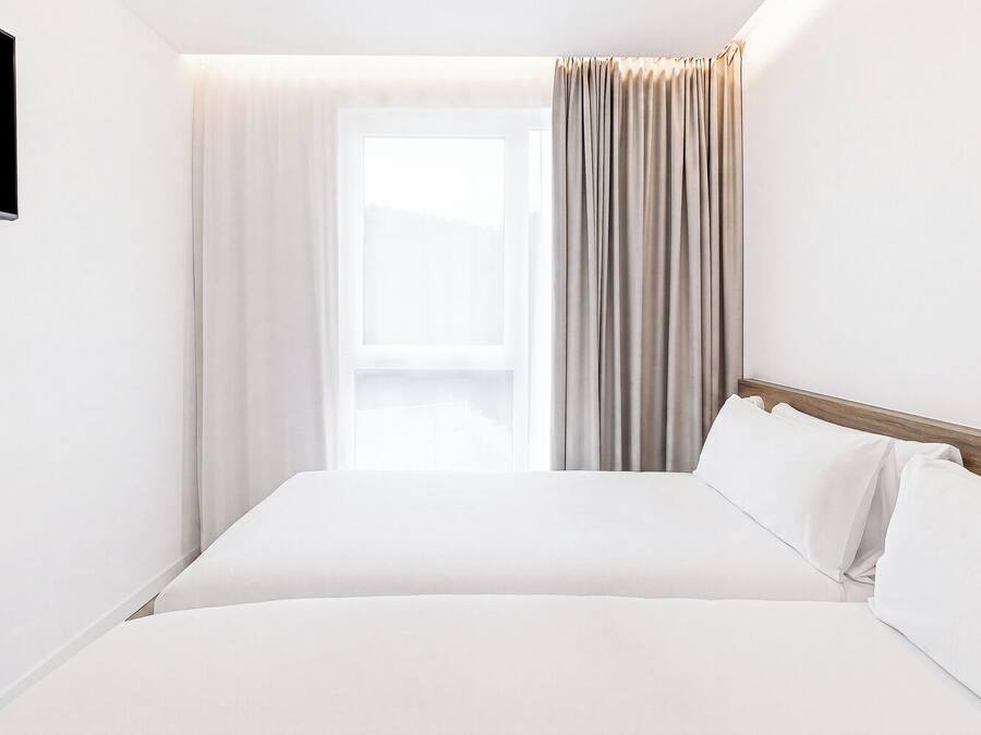 A hotel room with a bed, curtains, a TV, and a window.