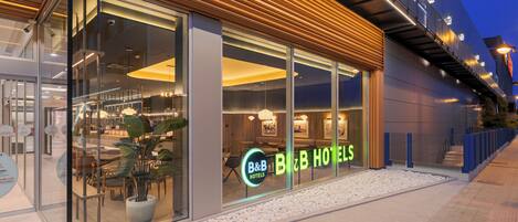 A hotel with a modern facade, large glass windows, and a neon sign.