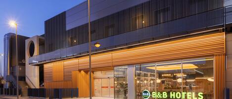 A modern hotel with a prominent B&B sign, a covered entrance, and a staircase leading to an upper level.