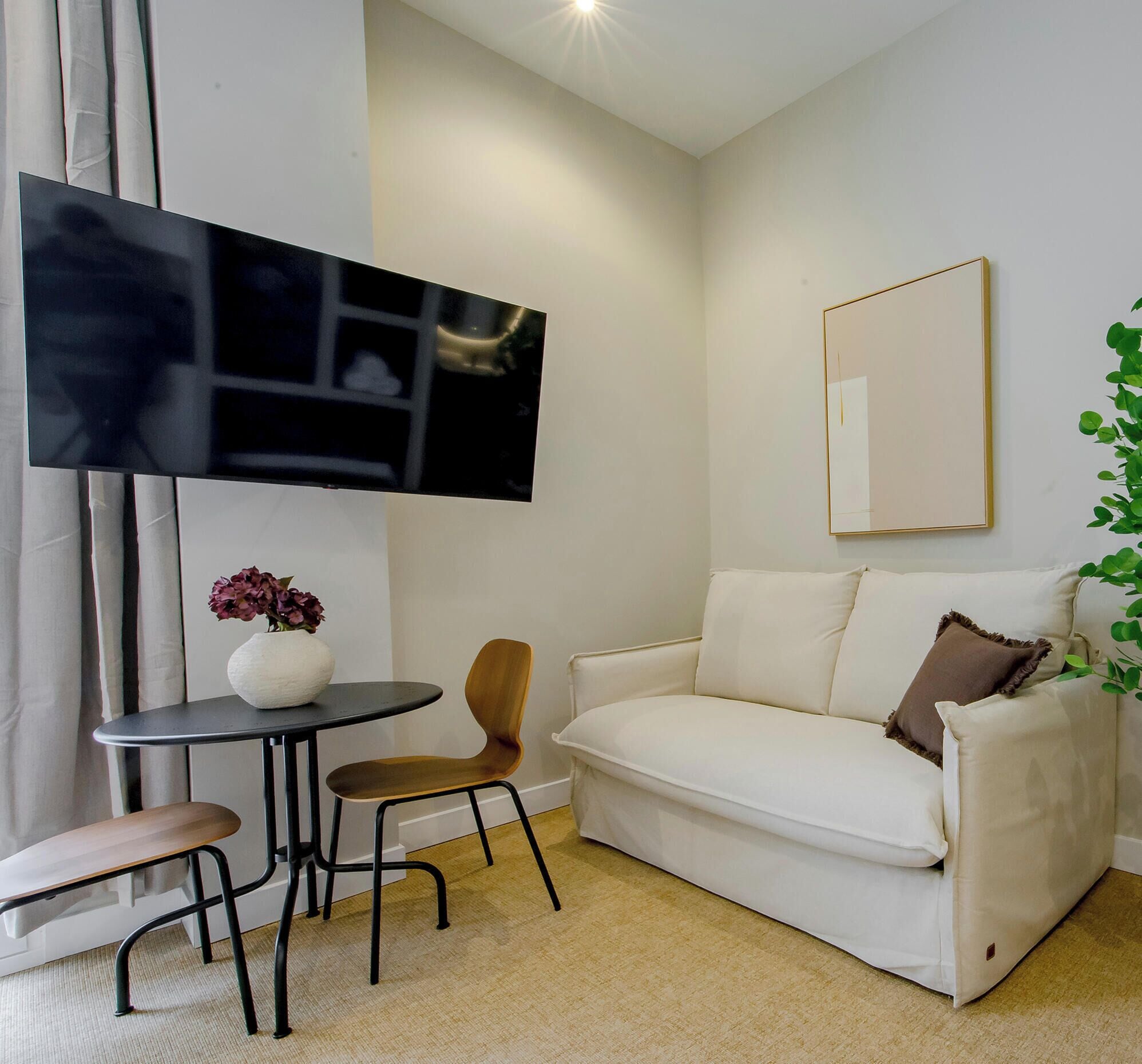 A modern living room with a white sofa, a small round table, a TV mounted on the wall, and a mirror.