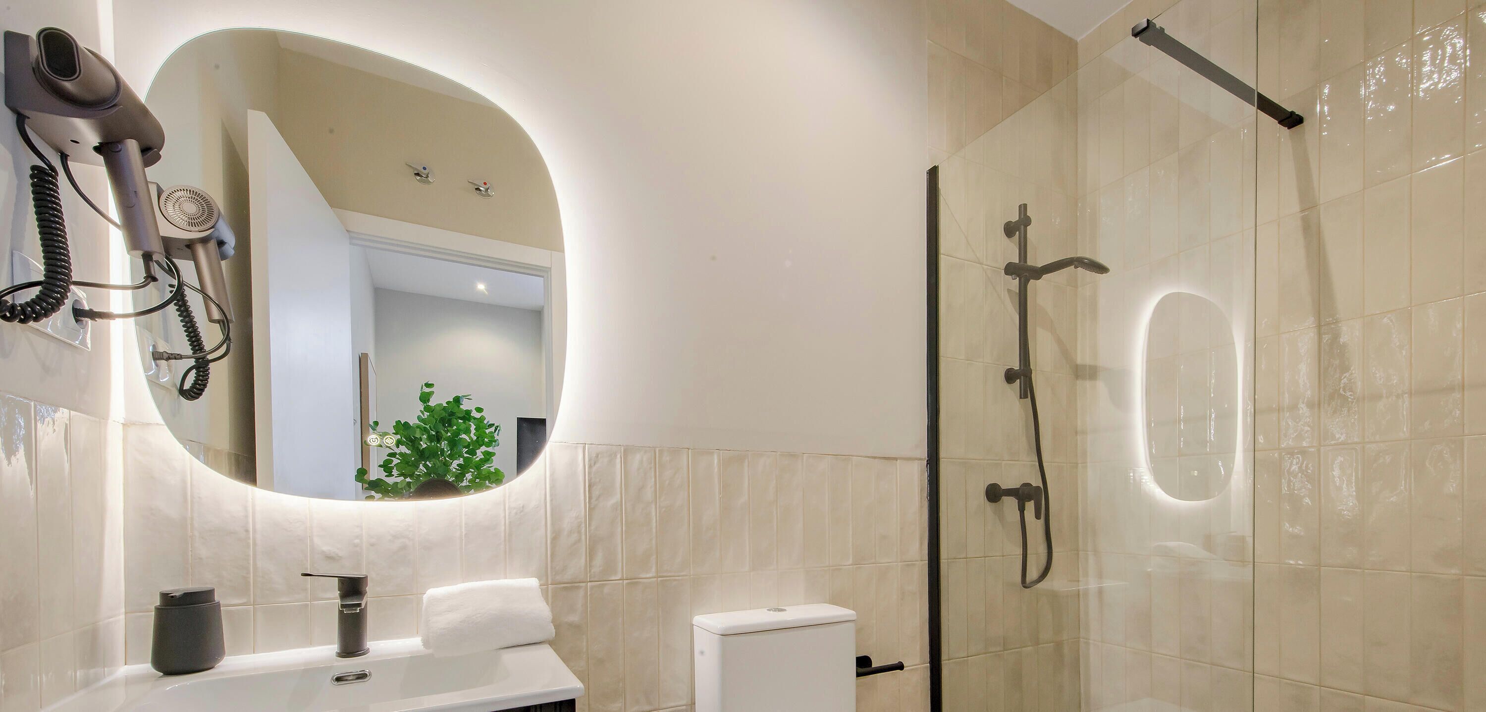 Un bagno moderno con uno specchio grande, un asciugacapelli, un water e un box doccia.