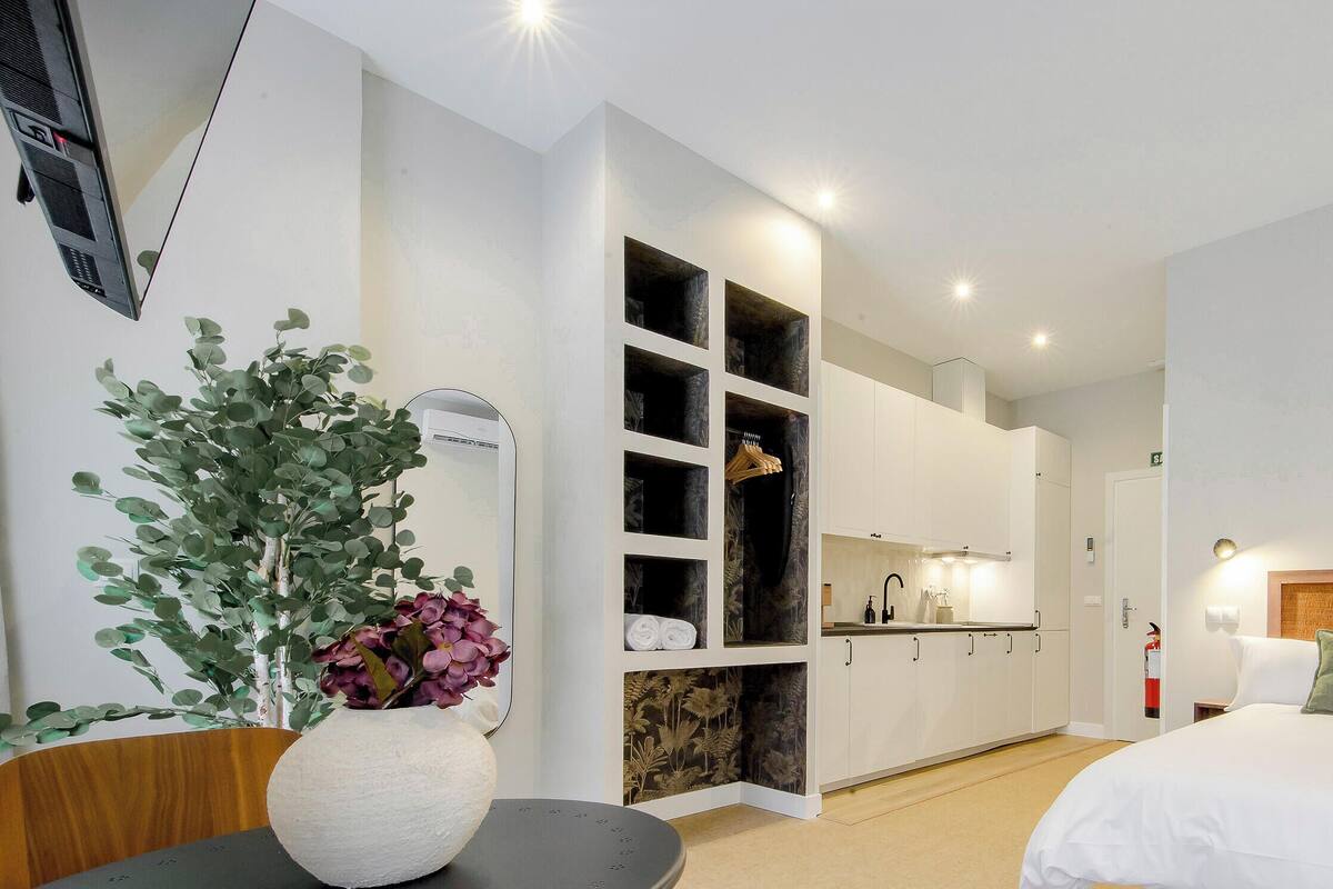 Una habitación de hotel con cama, kitchenette, baño y una planta en maceta.