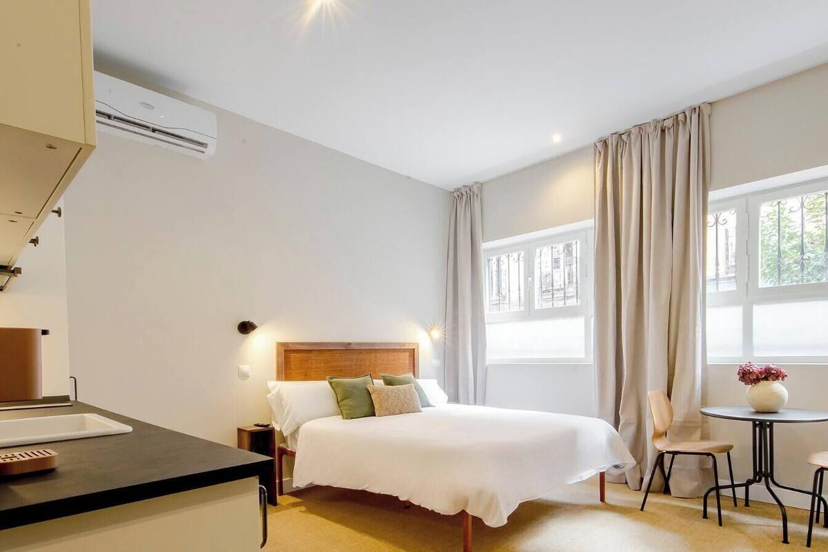 Habitación de hotel con cama, mesita de noche, silla y una pequeña mesa con un jarrón.