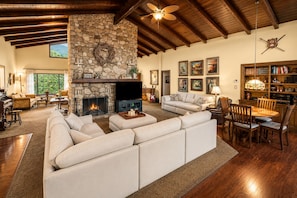 A spacious living room with a stone fireplace, a large sofa, a dining area with wooden chairs, and a bookshelf filled with books. - 25% Off Aug 27-30 Great 4 Families -Pool, Jacuzzi* (Fillmore)