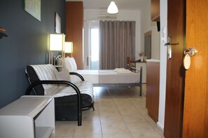 Una camera d'albergo con un letto, una sedia, una scrivania, una lampada e una porta.