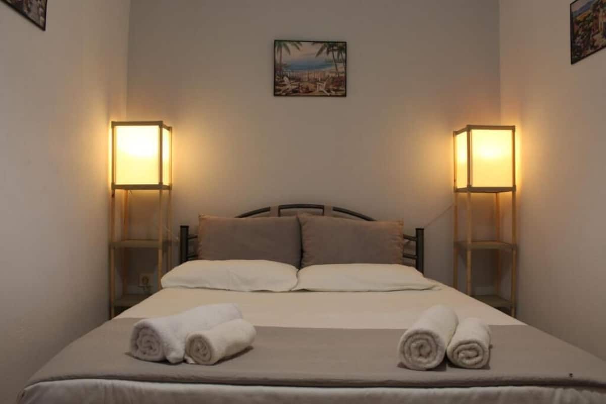 A hotel room with a bed, two bedside lamps, a painting on the wall, and rolled towels on the bed.