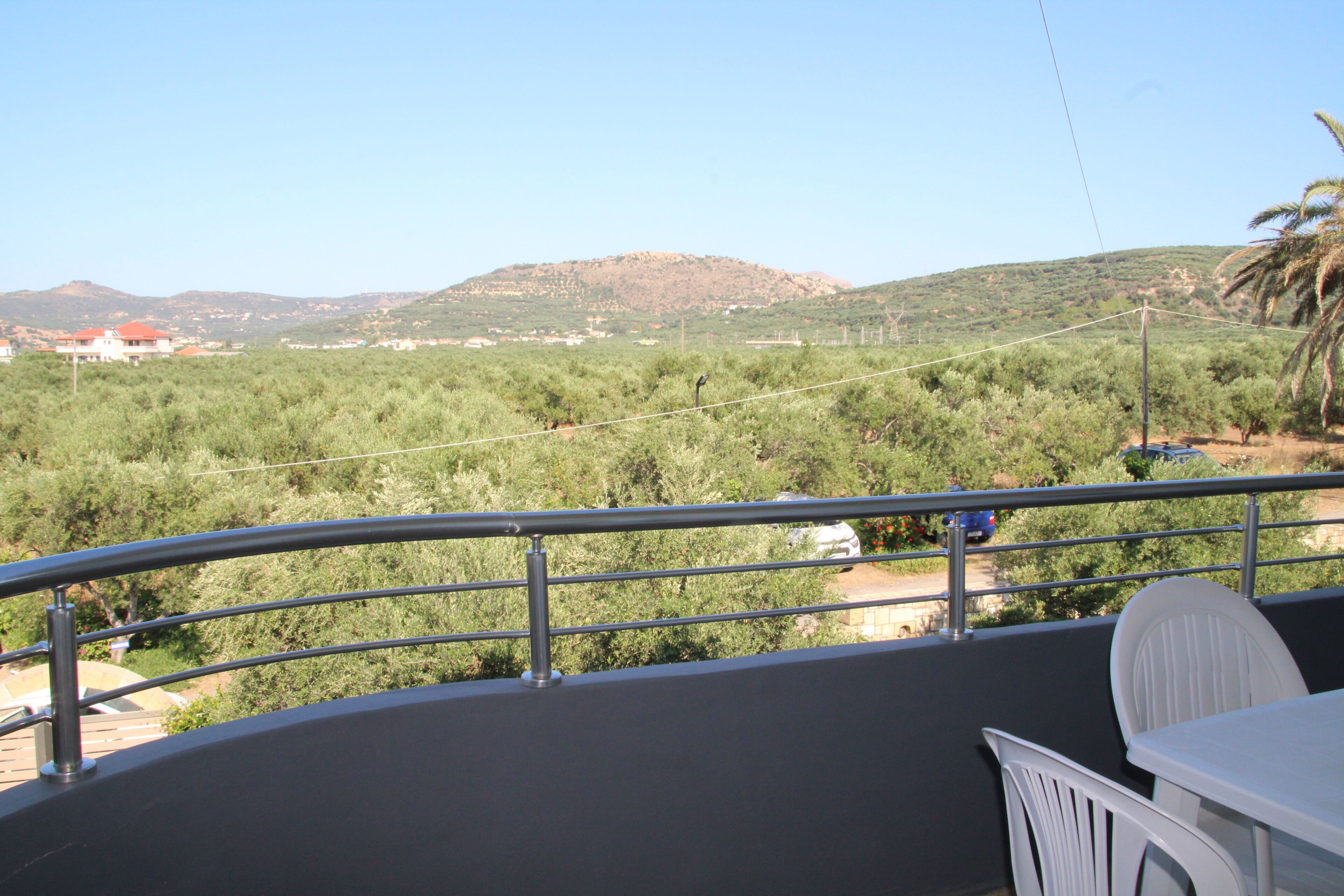 Un balcon donnant sur un paysage vallonné, une table blanche et une chaise blanche.