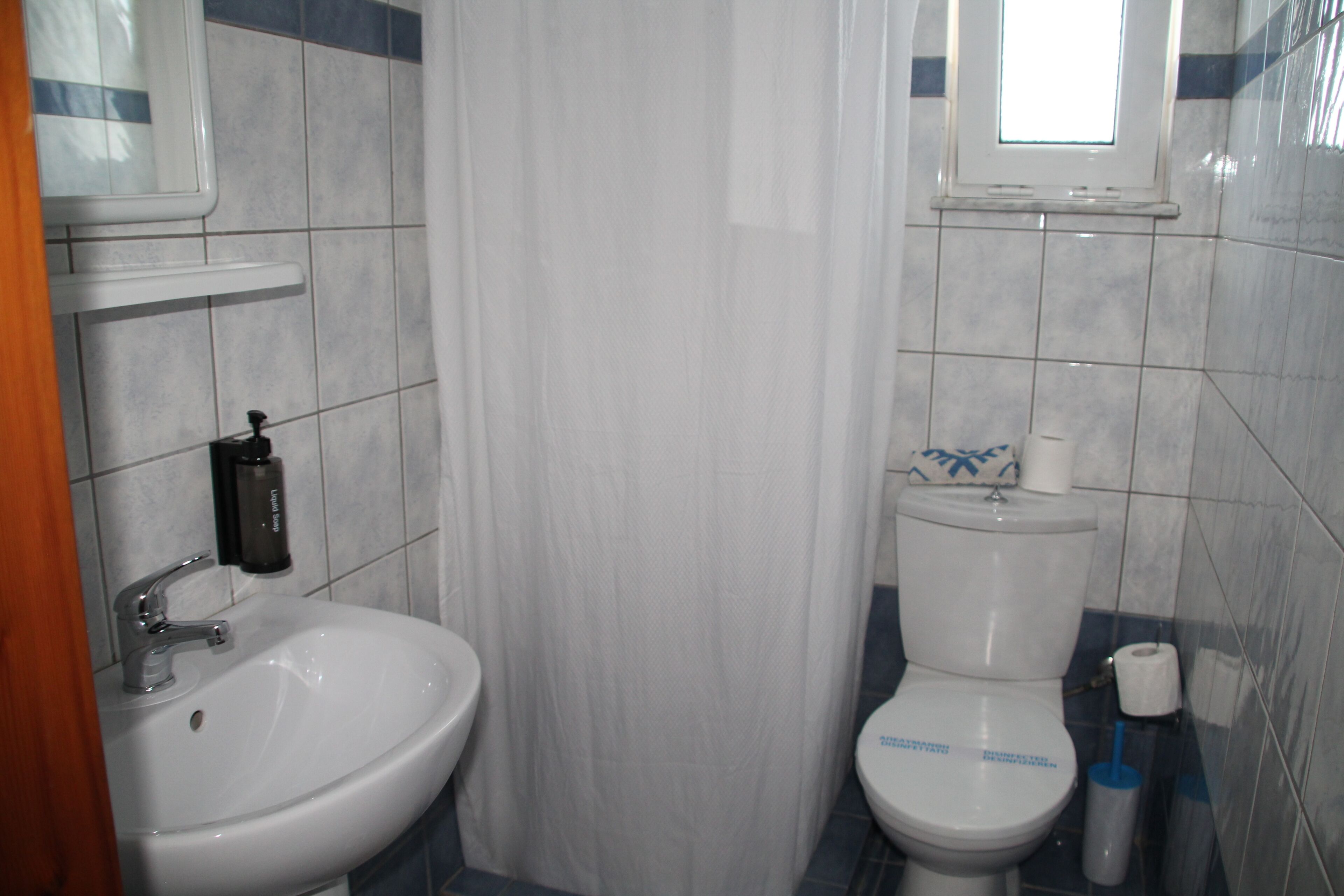 Un baño con lavamanos, inodoro y ventana sobre el inodoro.