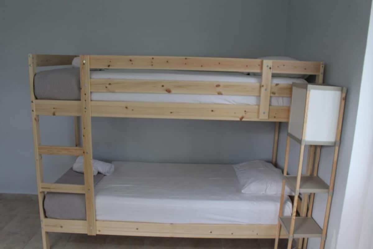 A bunk bed with a shelf on the right side, a pillow on the lower bunk, and a blanket on the upper bunk.