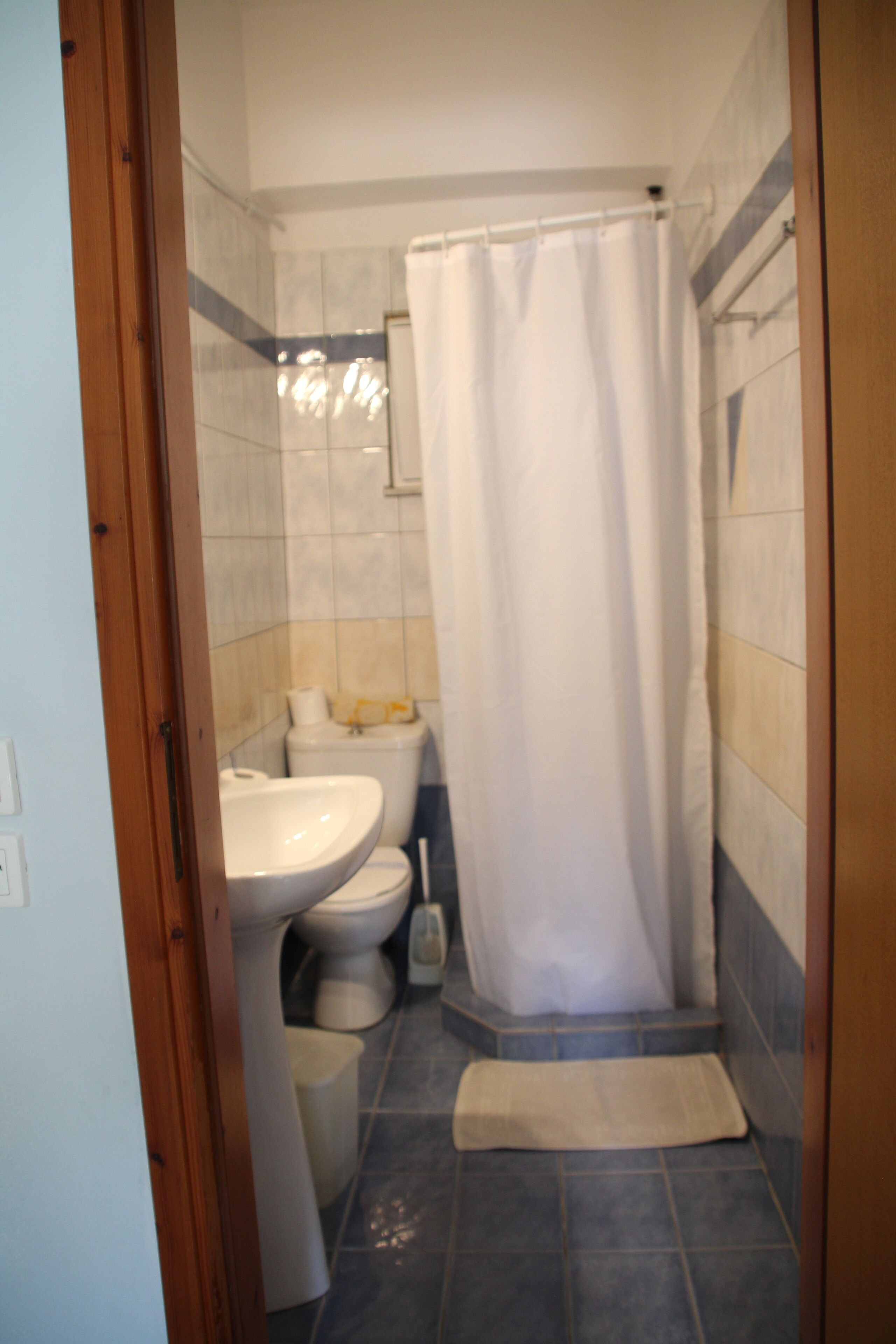 A bathroom with a shower curtain, a sink, a toilet, and a small rug on the floor.