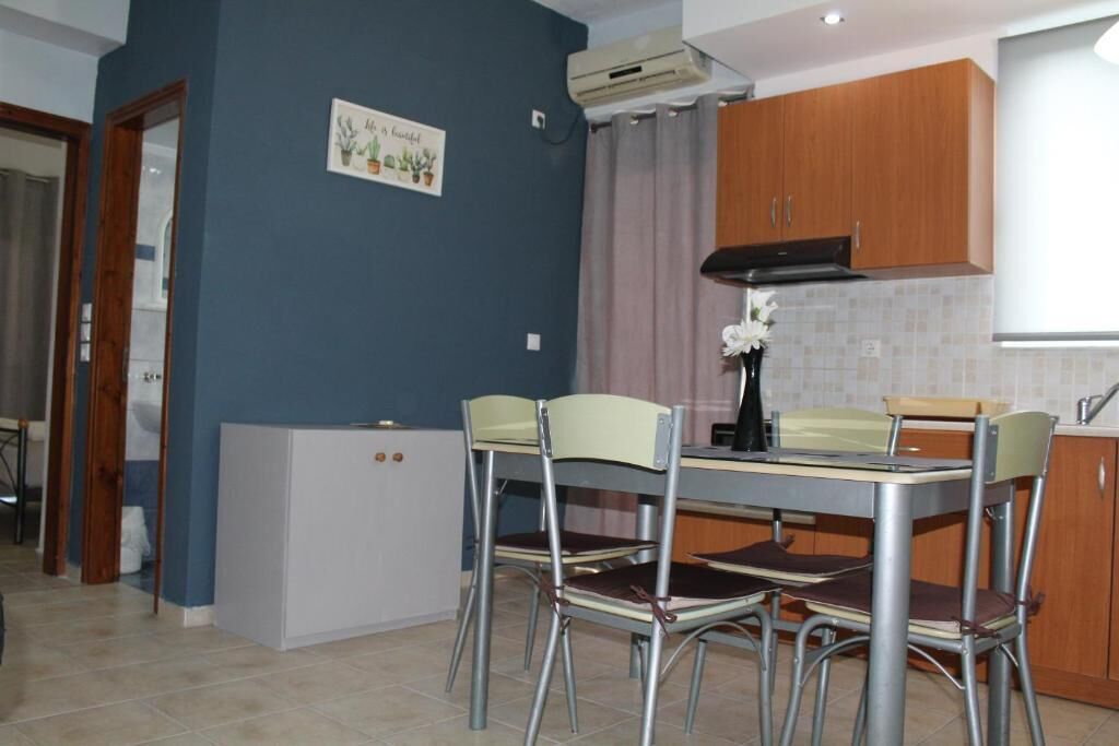 Une cuisine compacte comprenant une table et des chaises, un petit réfrigérateur, des meubles de rangement en bois et un climatiseur fixé au mur.