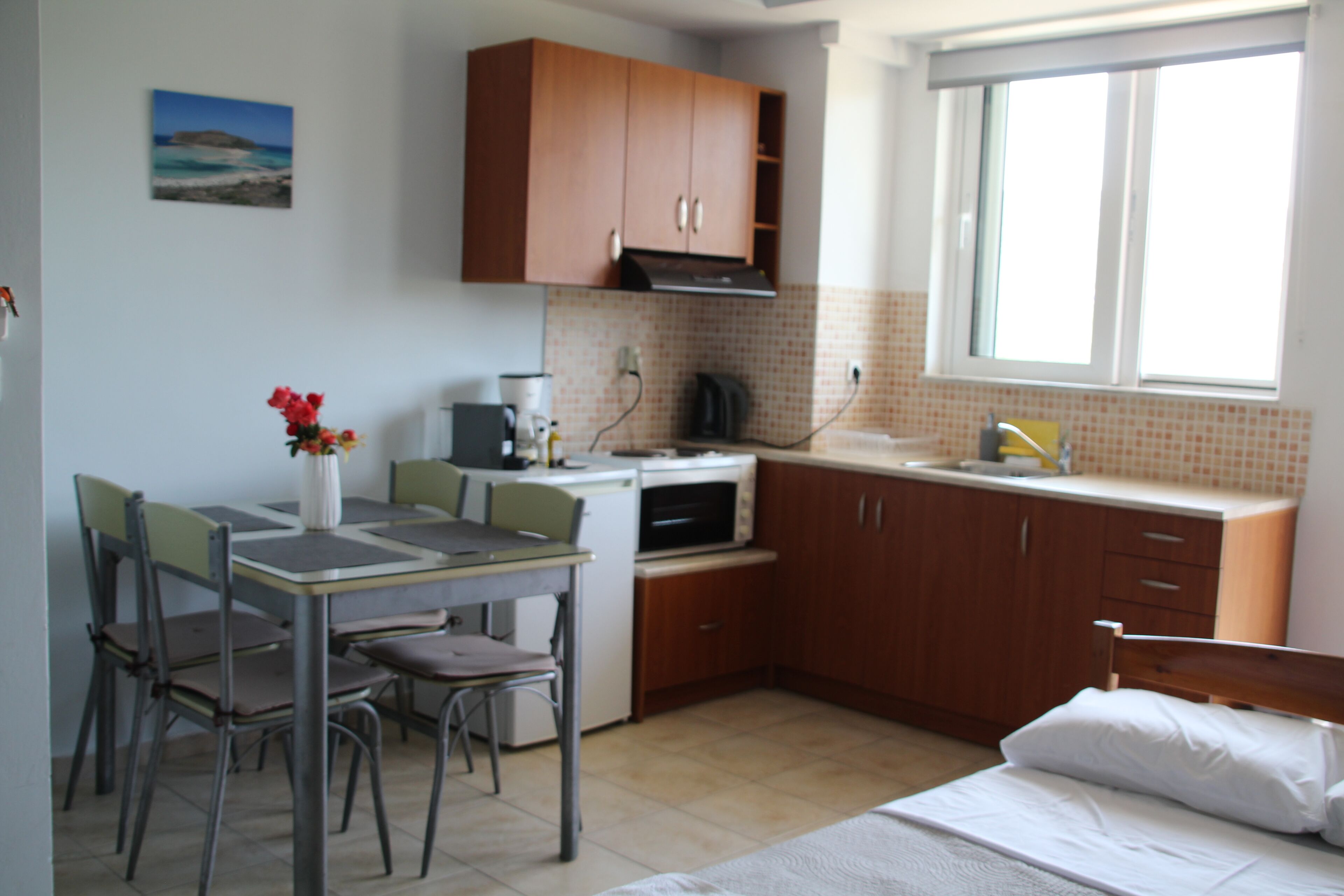A compact kitchen with a dining table, chairs, a bed, and a window.