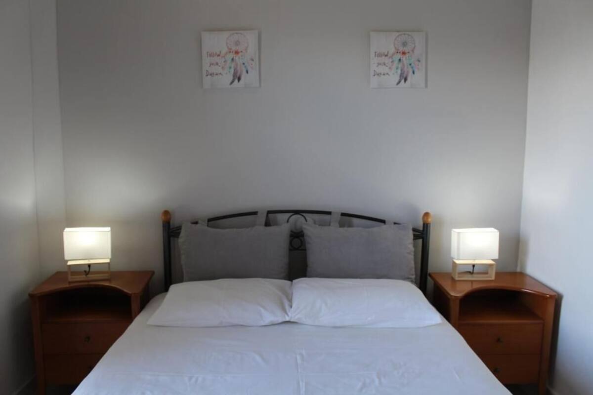 A bed with white linens, two bedside tables with lamps, and two wall-mounted dreamcatchers.
