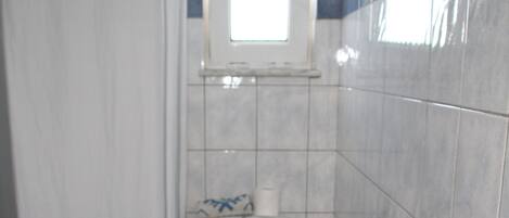 Un baño con inodoro, cortina de ducha, ventana y un cubo de basura.