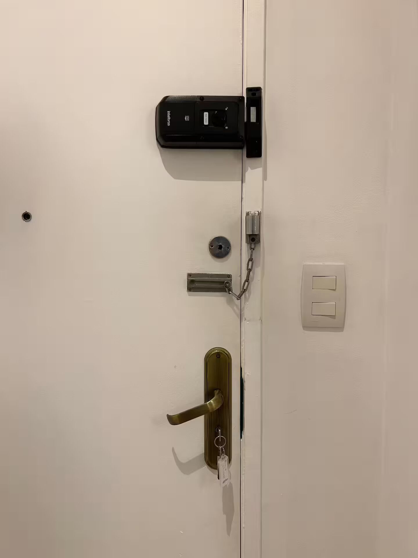 Een witte deur met een sleutelgat, een sleutelhanger, een slot, een sleutel en een lichtschakelaar.