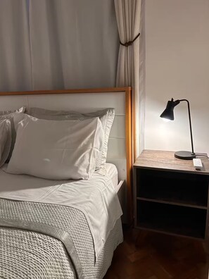 A neatly made bed with white linens, a wooden headboard, and a bedside table with a lamp and remote control. - Top apartment 350m from Copacabana beach (Rio de Janeiro)