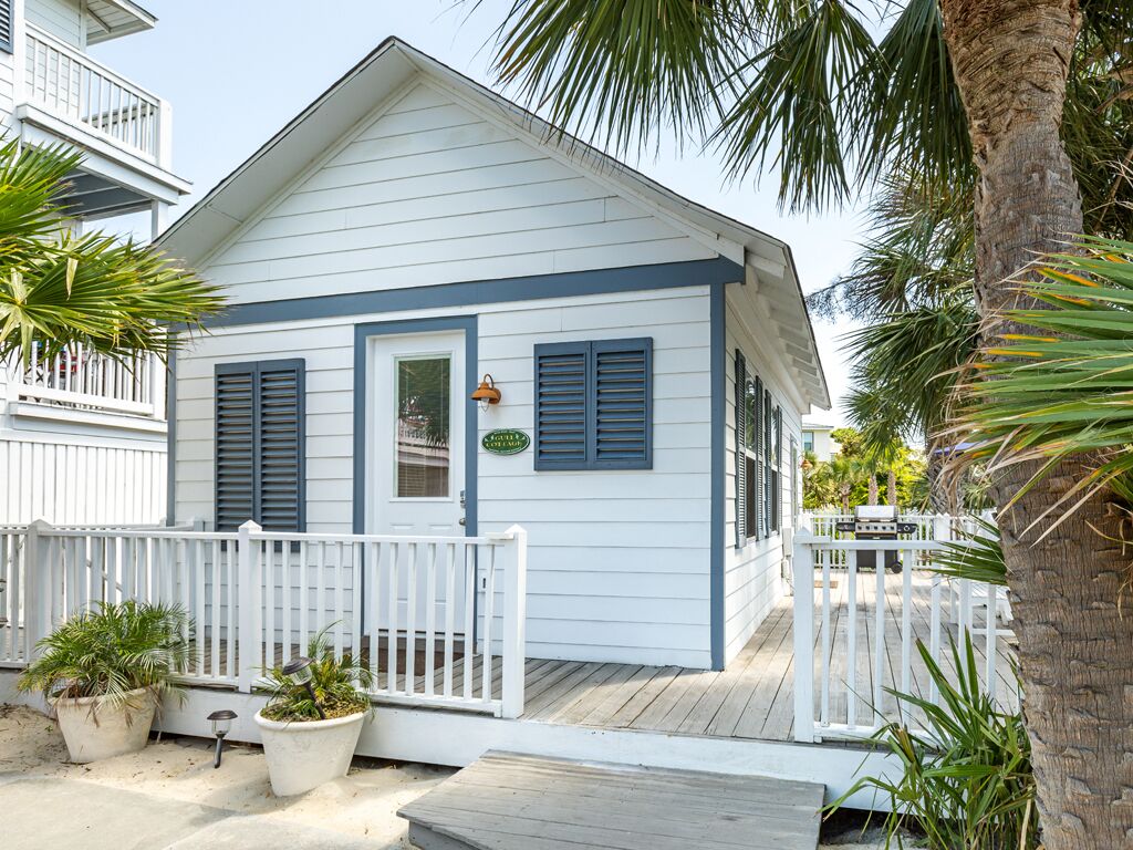 A coastal house with a white exterior, blue shutters, a wooden deck, and potted plants.