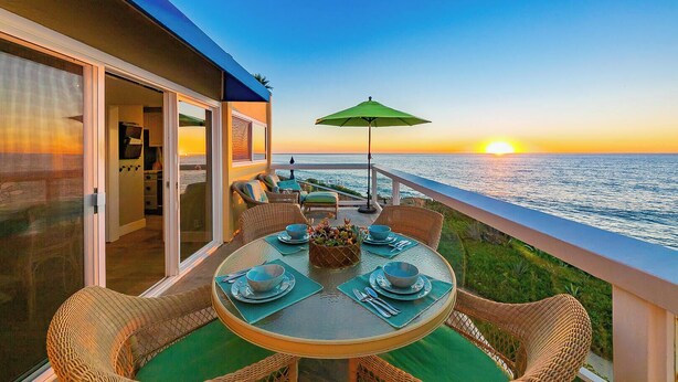 Ein Balkon mit Esstisch, der auf den Sonnenuntergang über dem Meer blickt.