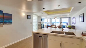 A modern kitchen with a dishwasher, a dining area with a table and chairs, and a view of the ocean through large windows. - 30+ Stay! Oceanfront, Great For Families W/Parking (San Diego)