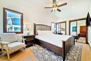 Quarto com cama, cadeira, mesa de cabeceira, abajur, ventilador de teto e uma grande janela.