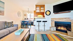 Ein modernes Wohnzimmer mit einer Couch, einem Couchtisch, einem Kamin und einer Küche im Hintergrund.