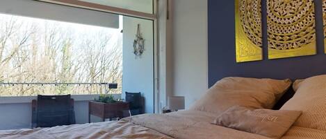 A bedroom with a large bed, a window with a view of trees, and decorative wall art.