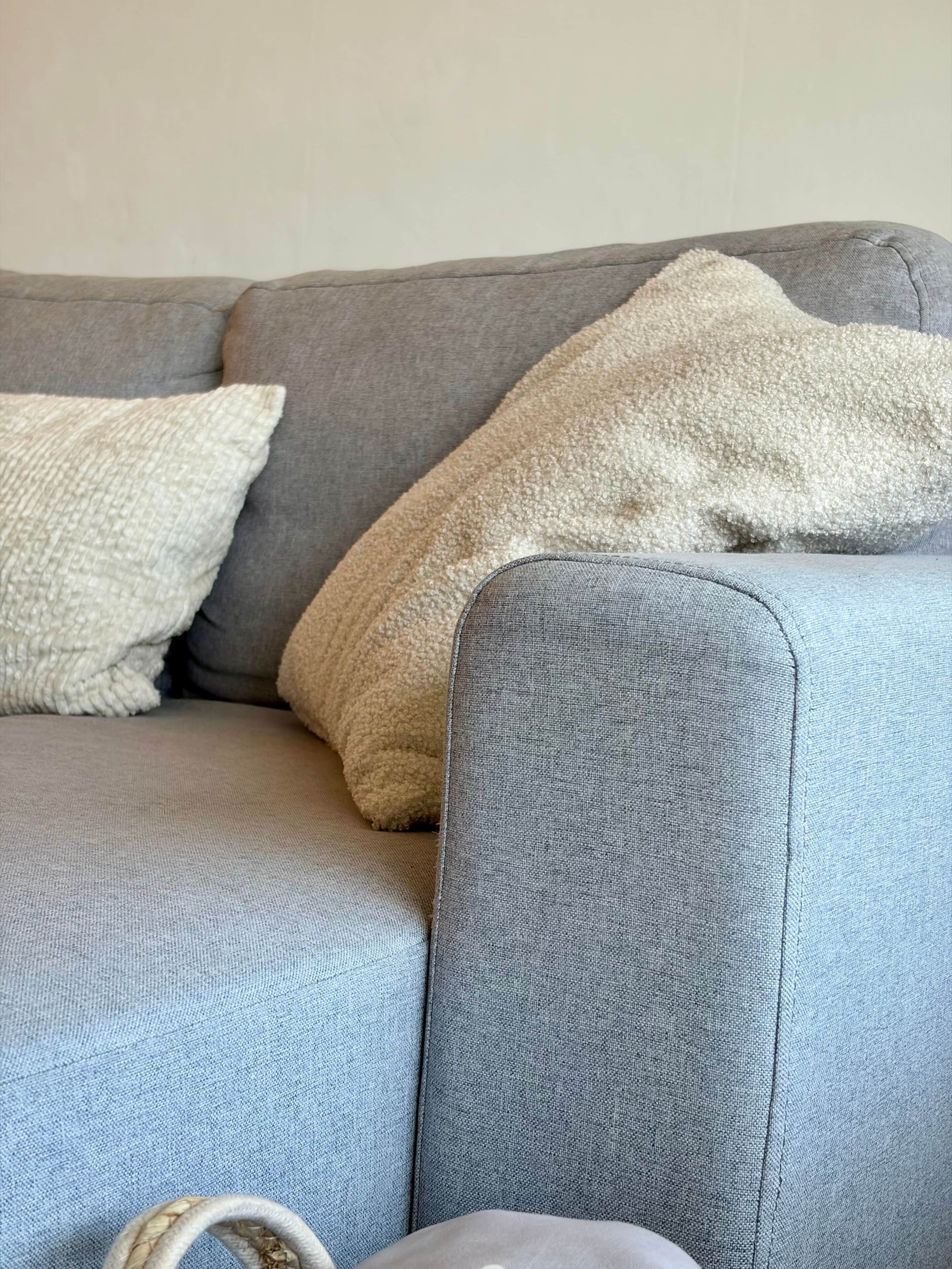 Un canapé gris recouvert d’un tissu texturé, un coussin blanc tricoté et un coussin beige moelleux.