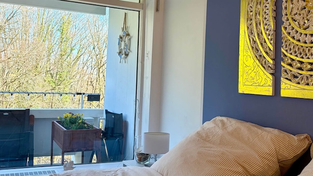 Un dormitori amb un llit gran, una finestra amb vista a arbres i decoració mural.