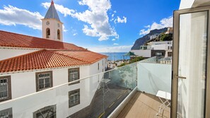 Ein Balkon mit Glasgeländer mit Blick auf eine Küstenstadt, eine Kirche mit roten Ziegeldach und einem strahlend blauen Himmel.