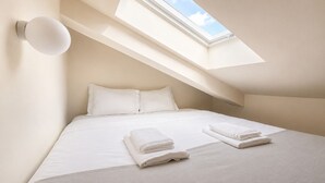 Een slaapkamer met een dakraam, een bed met witte lakens en twee opgevouwen handdoeken op het bed.