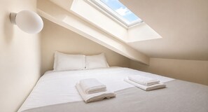 Ein Schlafzimmer mit Oberlicht, einem Bett mit weißen Leintüchern und zwei gefalteten Handtüchern auf dem Bett.