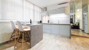 A modern kitchen with a marble countertop, white cabinetry, and a built-in island with bar stools. - Suites Garden (Las Palmas de Gran Canaria)