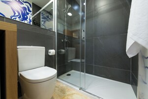 A modern bathroom with a toilet, a glass-enclosed shower, and dark tiled walls.