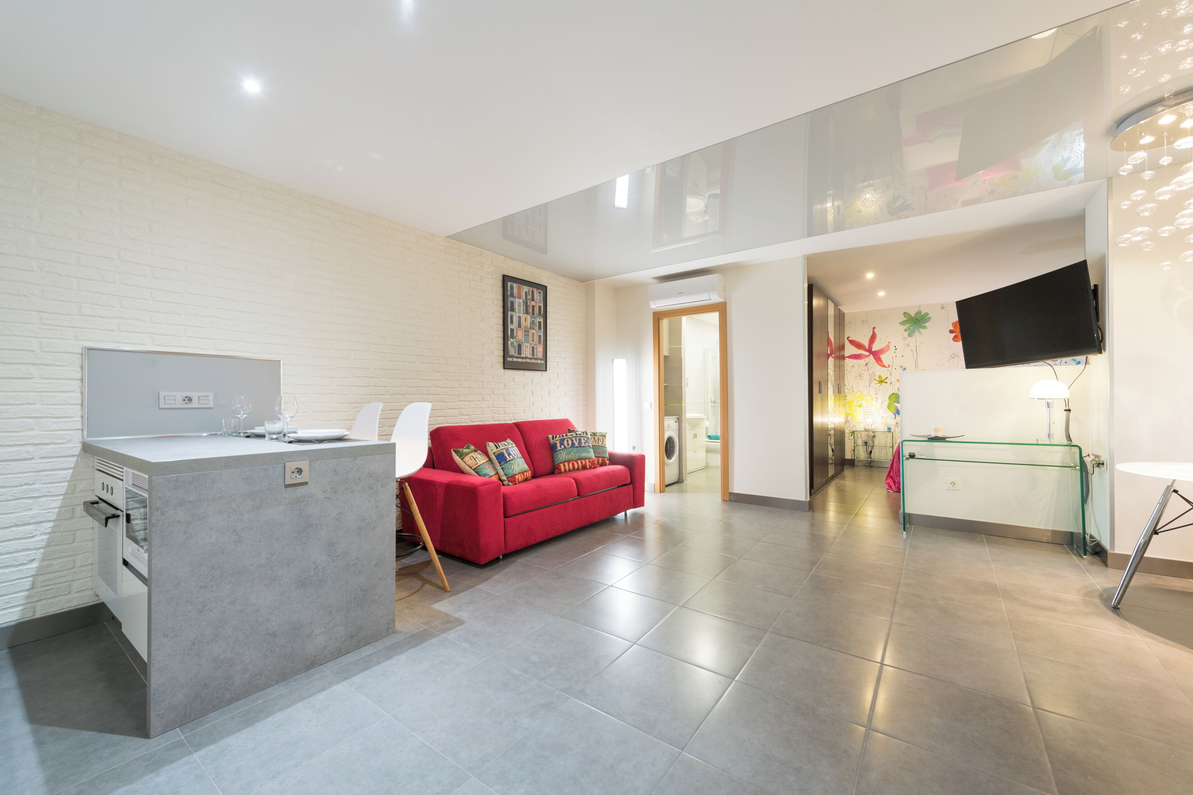 A modern kitchen with a built-in island, a red sofa, and a flat-screen TV mounted on the wall.